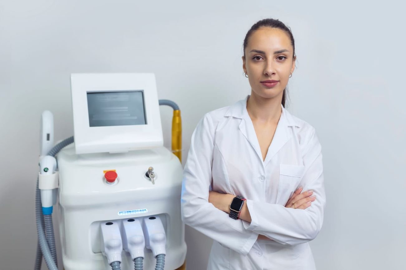 Female specialist in white coat standing next to professional laser skin treatment machine in a clinic setting